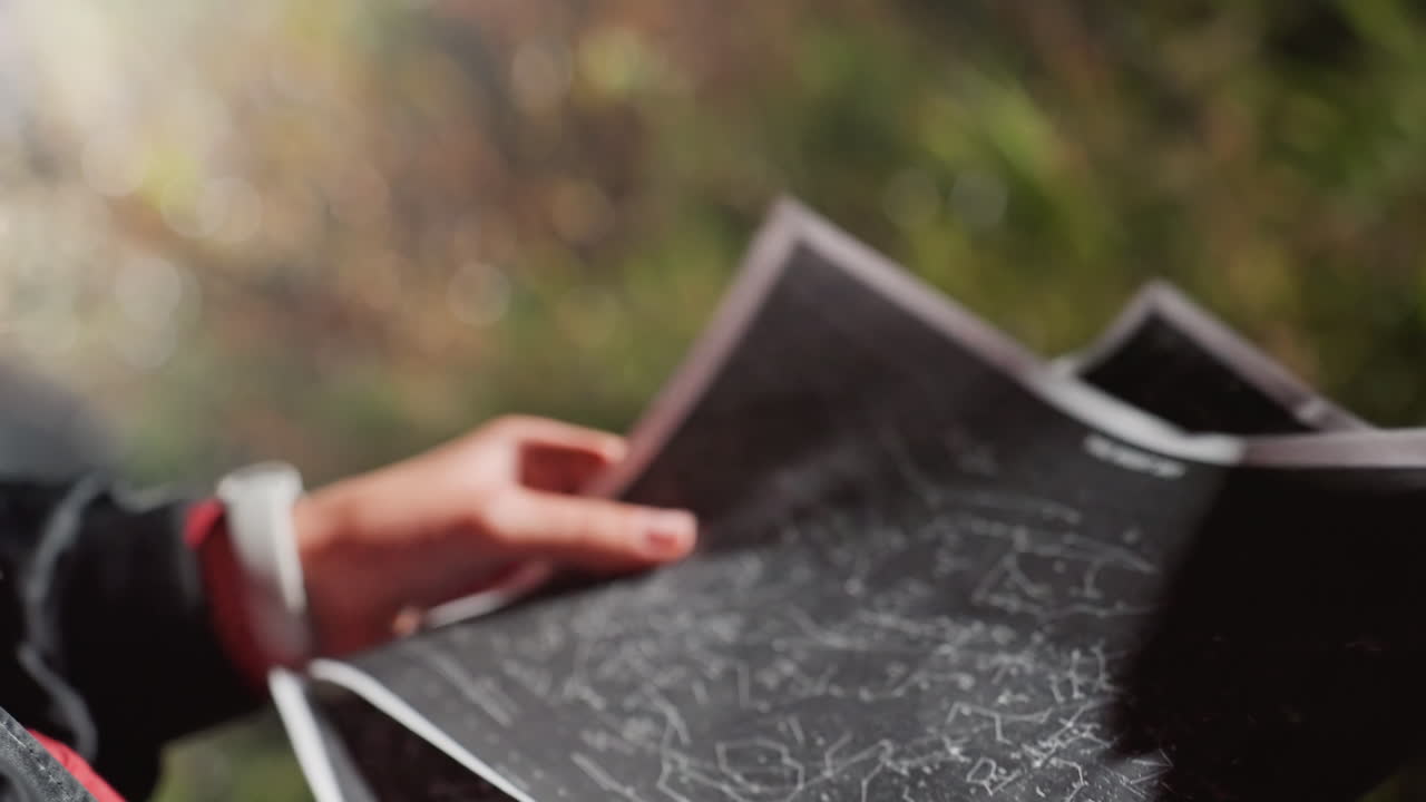 hands holding star chart marking constellations outdoors, closeup of hands annotating celestial map with pen, sunlight through foliage creating soft bokeh, researcher preparing telescope alignment
