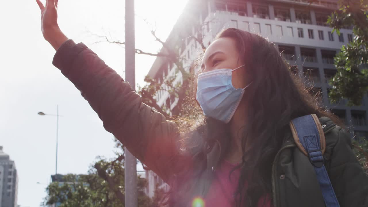 길거리에서 서 있는 동안 택시를 호출하는 얼굴 마스크를 착용 한 아시아 여성