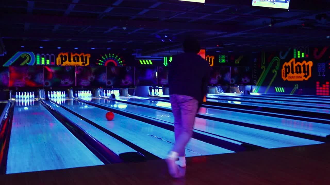 Mladý muž smíšeného původu hraje bowling v tmavé neonové bowlingové herně v arkádě.