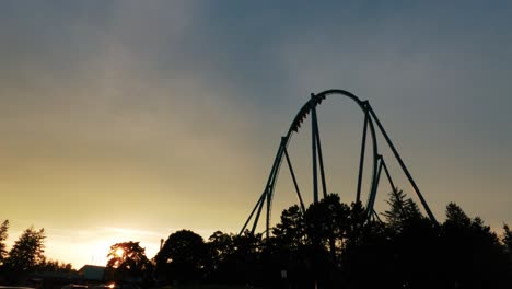 Slow-Motion-Roller-Coaster-Thrill-Ride-during-Sunset-Backlit-by-Sky-Silhouette-in-Amusement-Theme-Park-4K