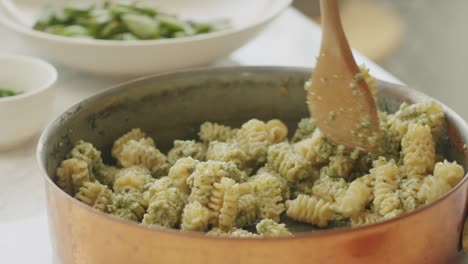 cocinero de cultivos agregando salsa de pesto en olla con pasta