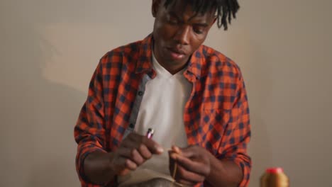 Focused-african-american-craftsman-wearing-apron-working-precisely-in-leather-workshop