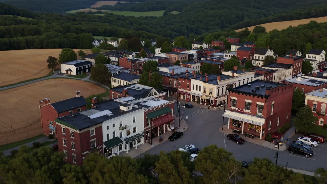 Aerial video captures a scenic landscape with rolling hills, fields, and a quaint village, viewed