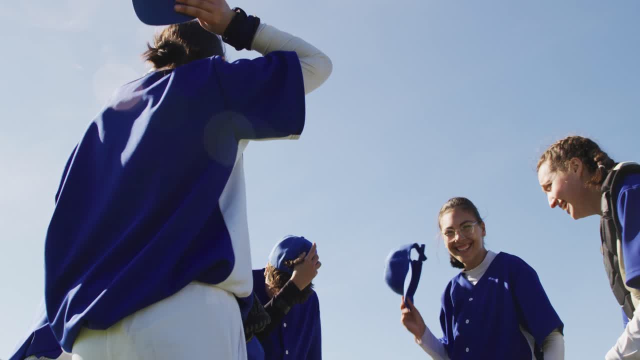 Happy diverse team of female baseball players throwing caps in the air,celebrating after game