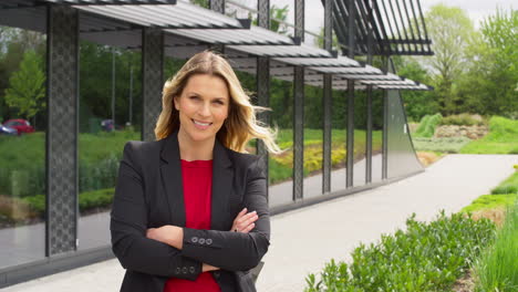 Portrait-Of-Smiling-Mature-Businesswoman-Standing-Outside-Modern-Office-Building