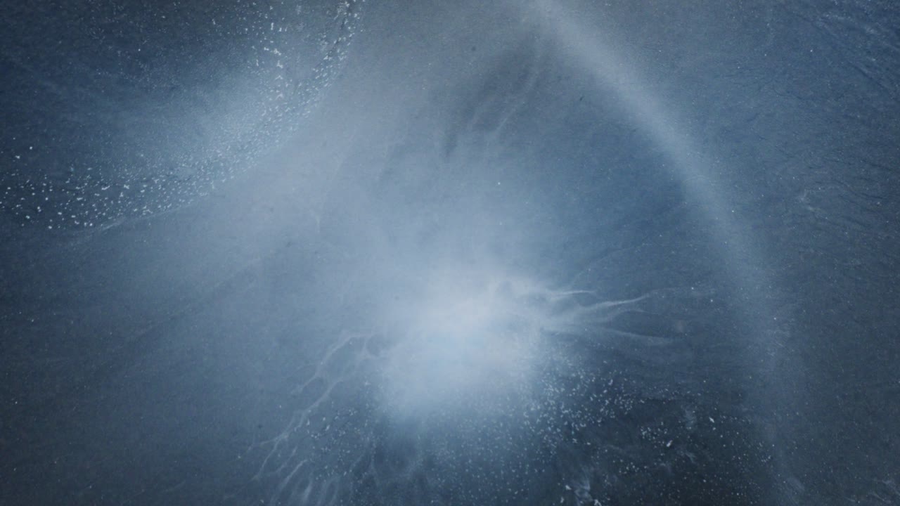 Whirling cloud of alcoholic ink in water forming a soft blue abstract pattern