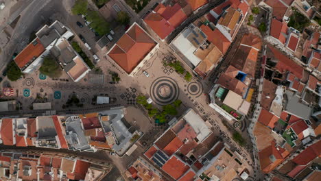 Gil-Eanes-square-and-rooftops-houses-in-Lagos,-Algarve,-Portugal,-aerial-birds-eye-overhead-top-down-view,-drone-rises-up-reveal-scenic-cityscape-with-people-walking-on-streets,-day