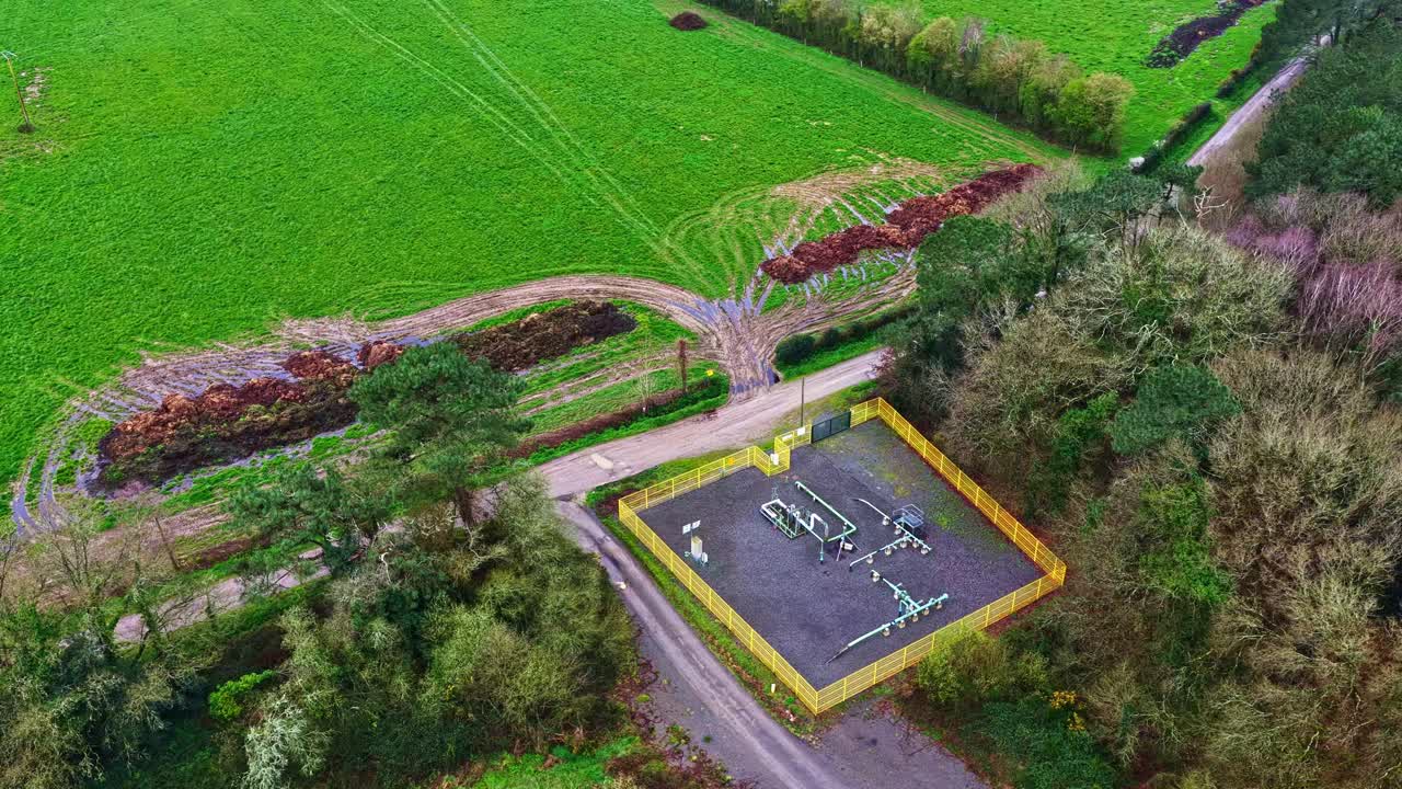 A small gas facility fenced in yellow, set amidst expansive green fields and dense trees. Suitable for discussions on energy infrastructure or rural development