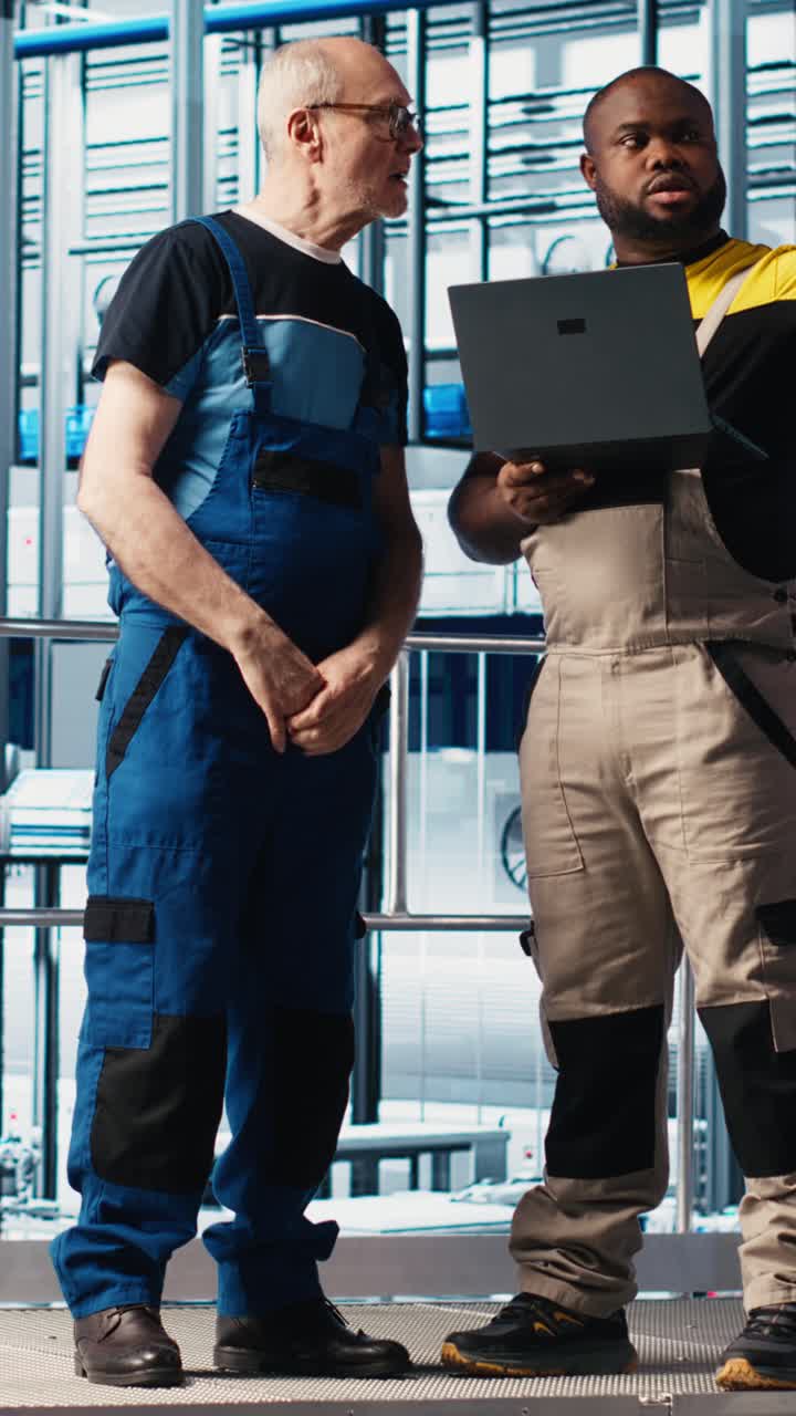 Vertical video Senior engineer talks with intern in smart factory, helping trainee use software