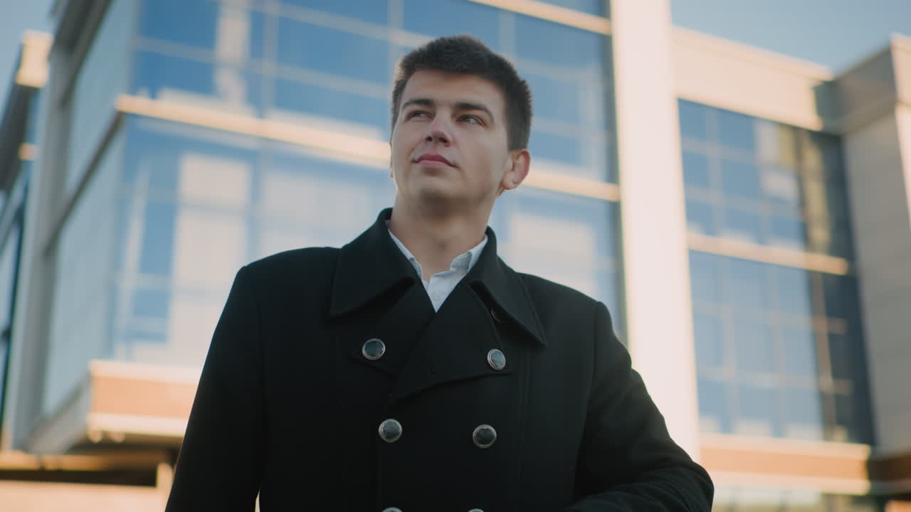 검은 옷을 입은 남자가 미묘한 미소를 지으며 손목 시계를 확인하면서 멀리 바라보고, 자신감과 평온을 발산합니다. 배경에는 현대적인 유리 건물이 남자의 빛을 반사합니다.