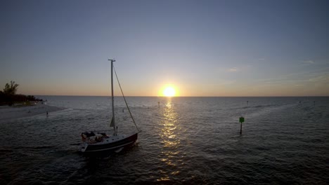 aerial 4k drone footage of a yacht sailing out into the gulf of mexico while the sun is setting over the horizon and reflection across the water
