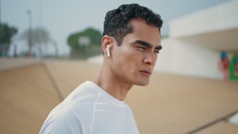 urban guy listening music in earphones closeup. handsome brunette looking camera