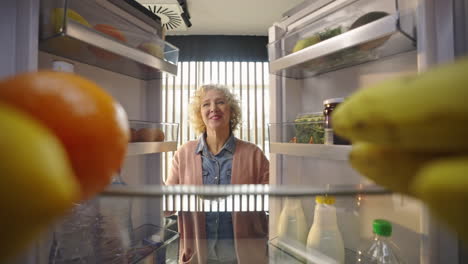 woman reaching into refrigerator for fruit
