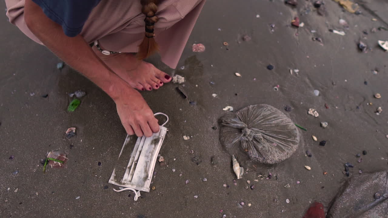 A woman feet walking on dark sand and picking up a wet mask on the ground, static shot
