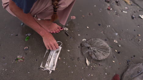 a woman feet walking on dark sand and picking up a wet mask on the ground, static shot