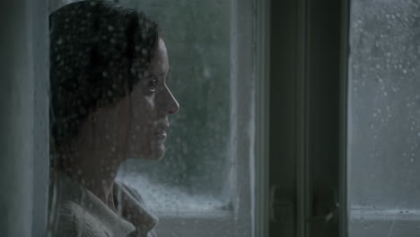 a woman looking out a rain-streaked window