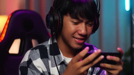 close up of asian teen boy gamer smiling to camera while playing video game on smartphone