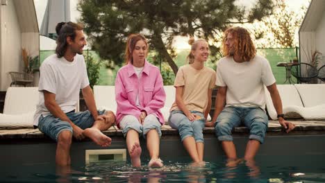 a company of four people is sitting near the sunbeds by the pool and talking among themselves. rest in the country house