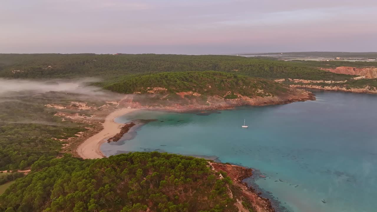 Volando sopra le nuvole al tramonto mentre si stendono sulle colline di una baia costiera isolata in Spagna.