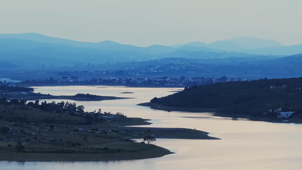 Blue hour glow spreads across dam and reservoir with rolling hills and countryside village in the distance, Valsequillo Puebla Mexico