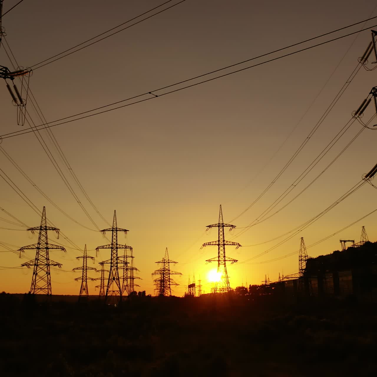 High-voltage power lines at sunset. Electricity distribution station. Tall high voltage electric transmission towers. Camera motion forward.
