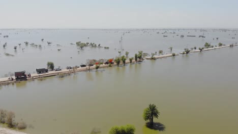 vuelo aéreo hacia la carretera con una línea de automóviles y camiones rodeados de un paisaje inundado en jacobabad, sindh
