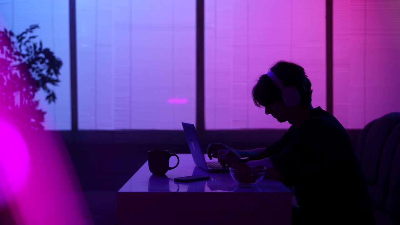 Person Silhouetted Eating and Working on Laptop at Night
