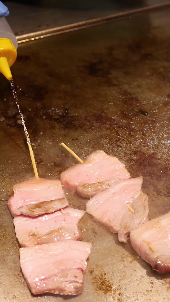 Seorang koki menuangkan minyak ke atas sate daging sapi wagyu dan menutupinya dengan tutup logam.