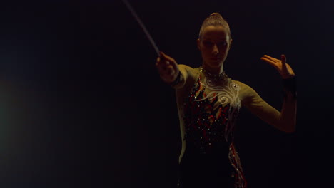 girl performing with flying ribbon for camera. gymnast rehearsing in dark hall.