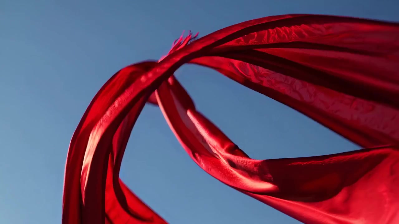 Tessuto rosso vibrante che fluttua con grazia contro un cielo azzurro limpido