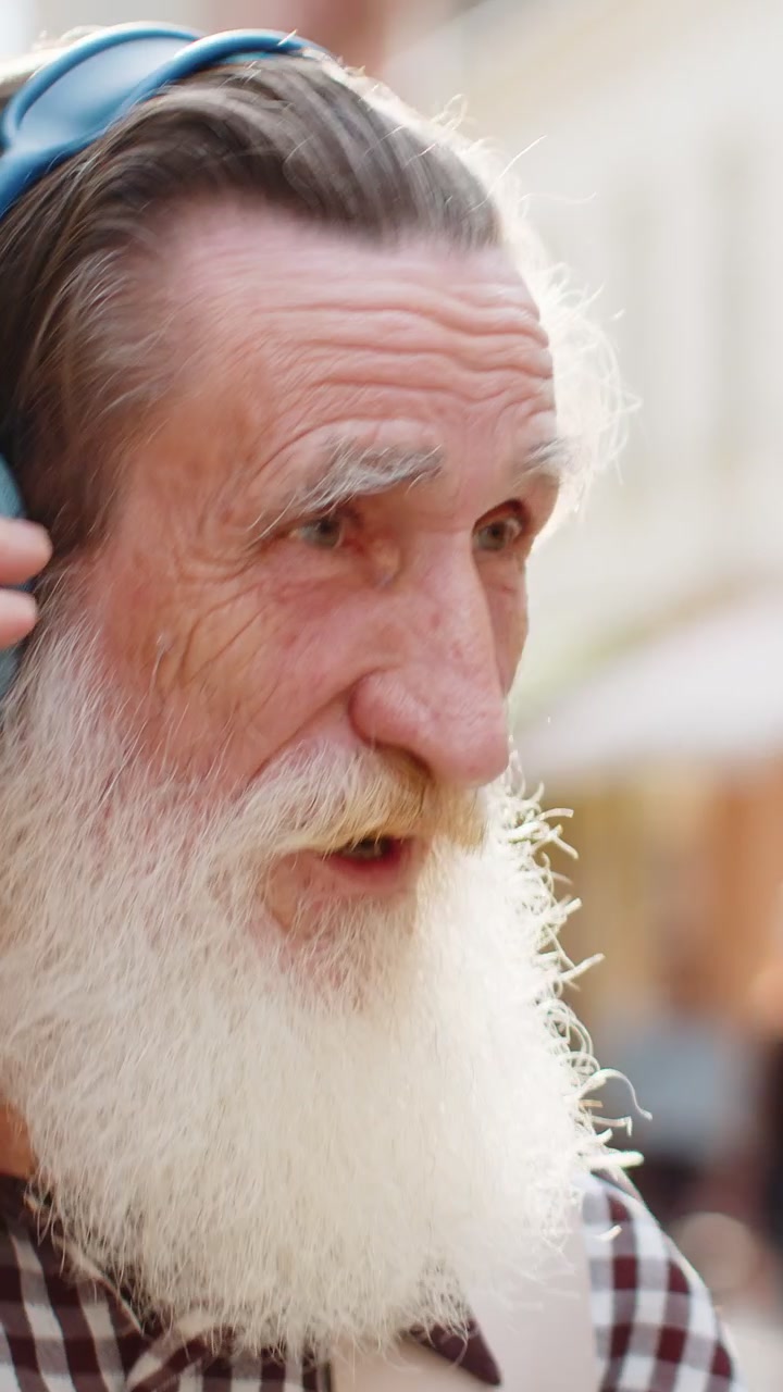 Vecchio anziano felice con le cuffie wireless che sceglie di ascoltare musica ballando all'aperto per la strada della città