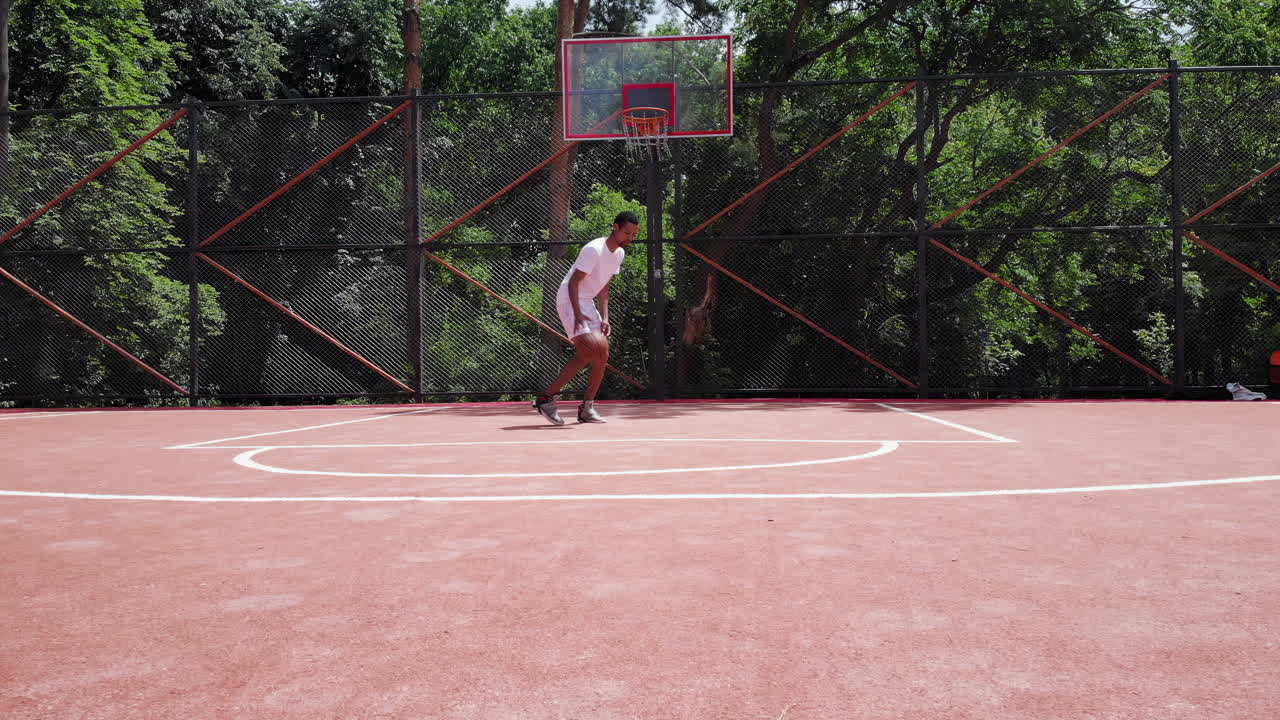 Chisinau, Moldova - September 10, 2021: A young athlete is practicing dribbling techniques on a red outdoor basketball court. The surrounding trees provide a natural backdrop while he focuses on his moves