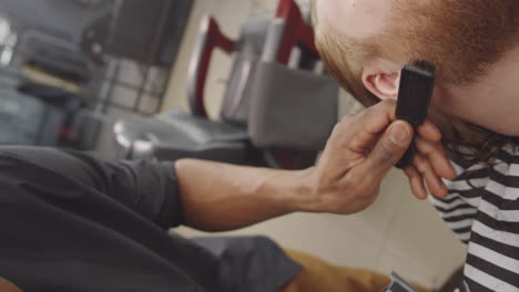 barber using trimmer and brush while shaving beard of client