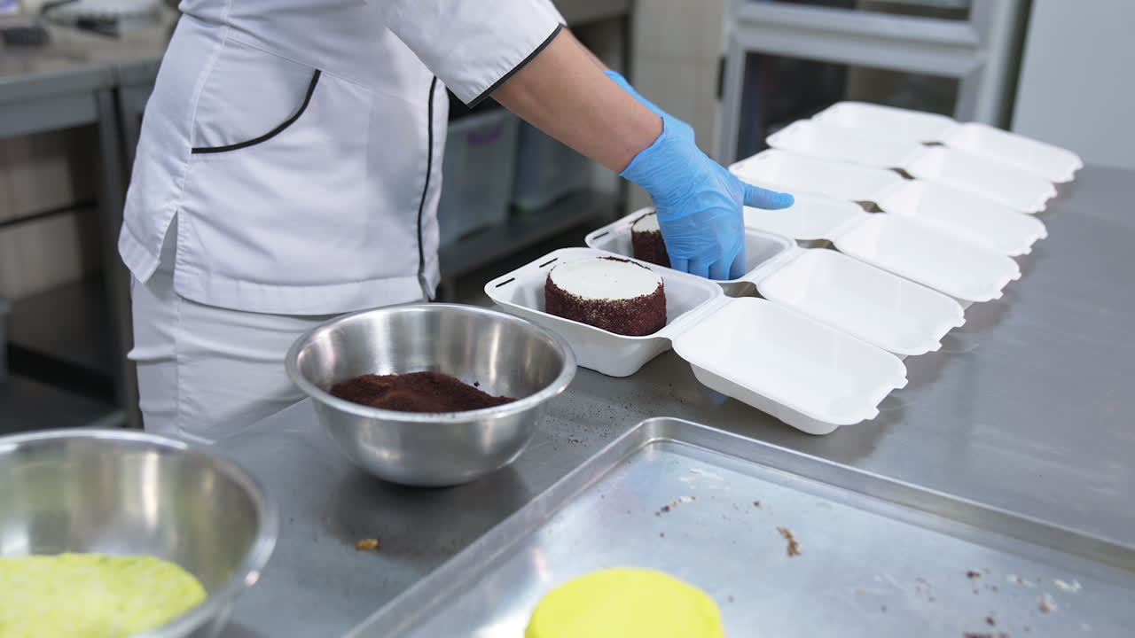 Cake production in the food factory. Confectioner puts the small cakes into individual packaging.
