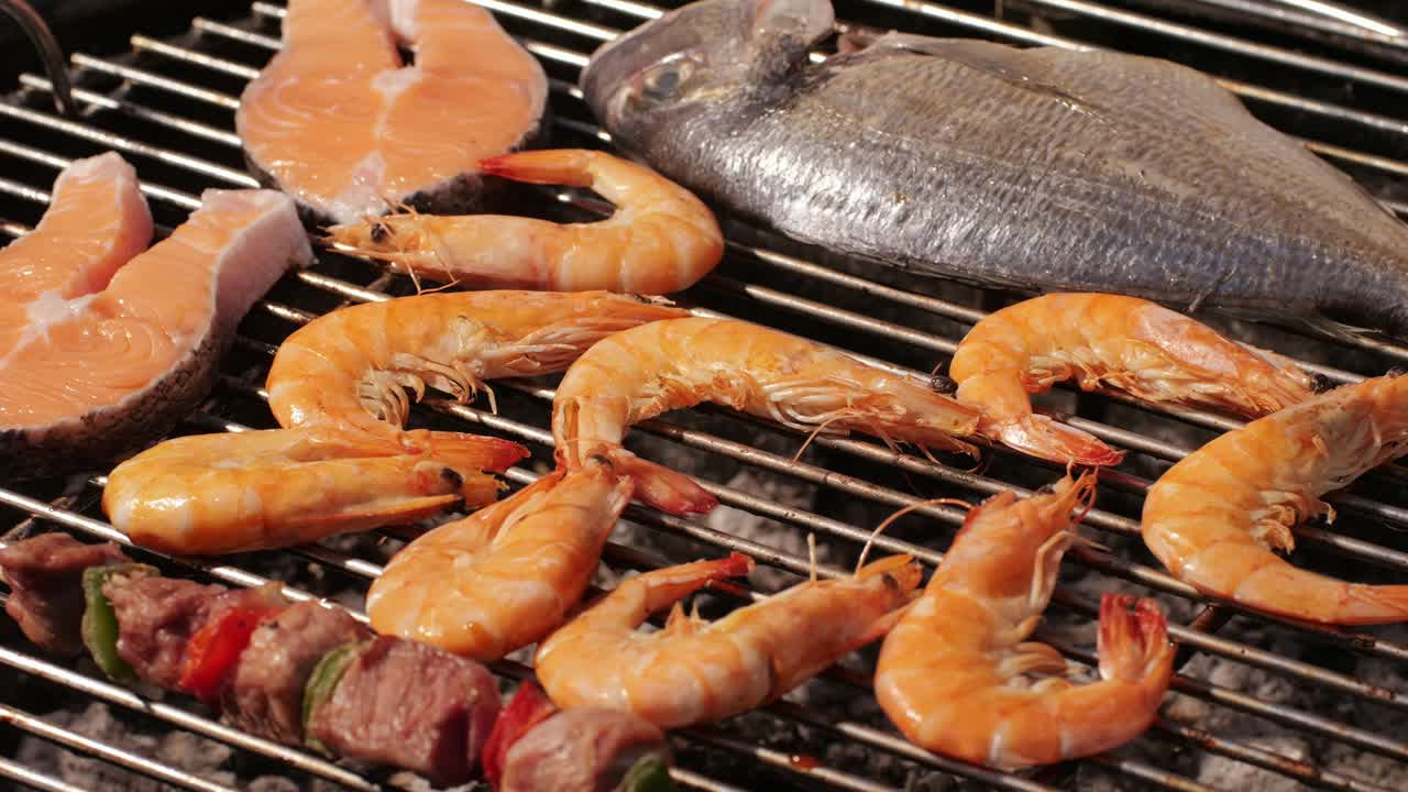 Chef cooking shrimps with oil and spices on grill close-up. Prawns on fire throwing them on pan. Dorado and salmon fish steak on frying grill. Restaurant Food concept. Sea food barbecue.