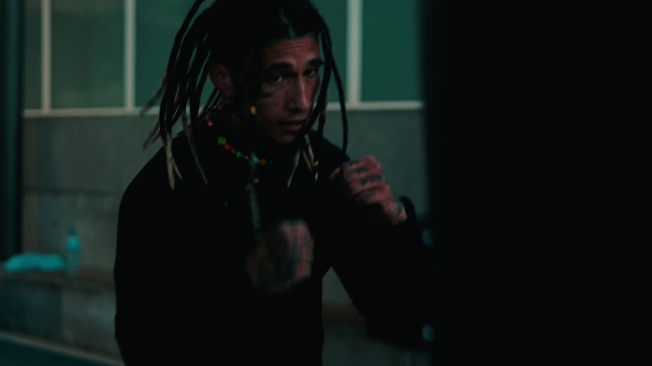 Mand med dreadlocks og ansigtstatoveringer ryster på hovedet og taler