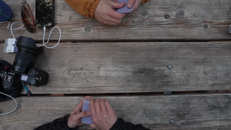 Two-young-men-playing-cards-on-a-picnic-table-while-camping