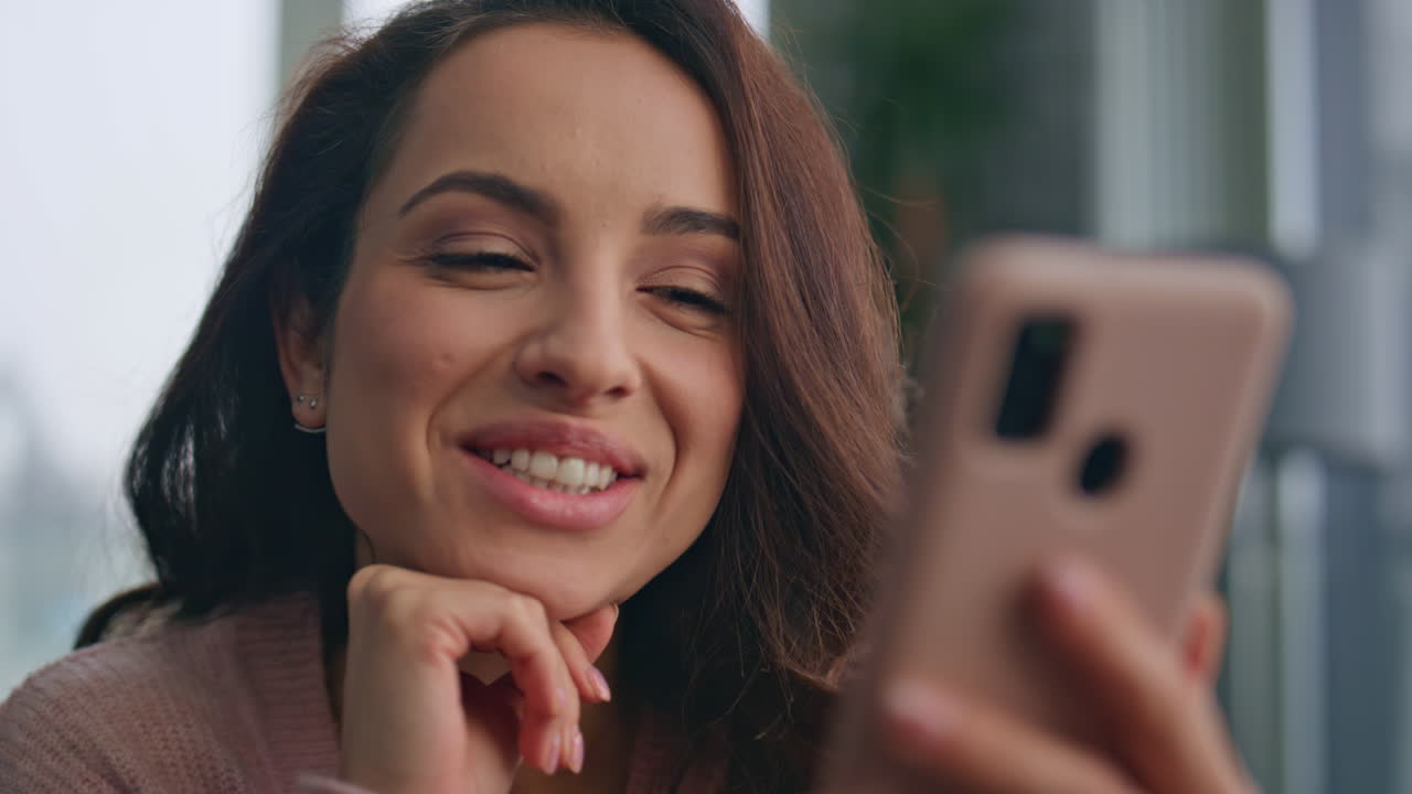 una morena feliz viendo un teléfono inteligente en primer plano en la sala de estar. una mujer soñadora recibe un sms