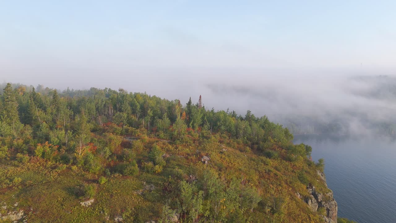 A pristine autumn day along Lake Superior highlights vertical cliffs and fiery forest tones under a clear blue sky