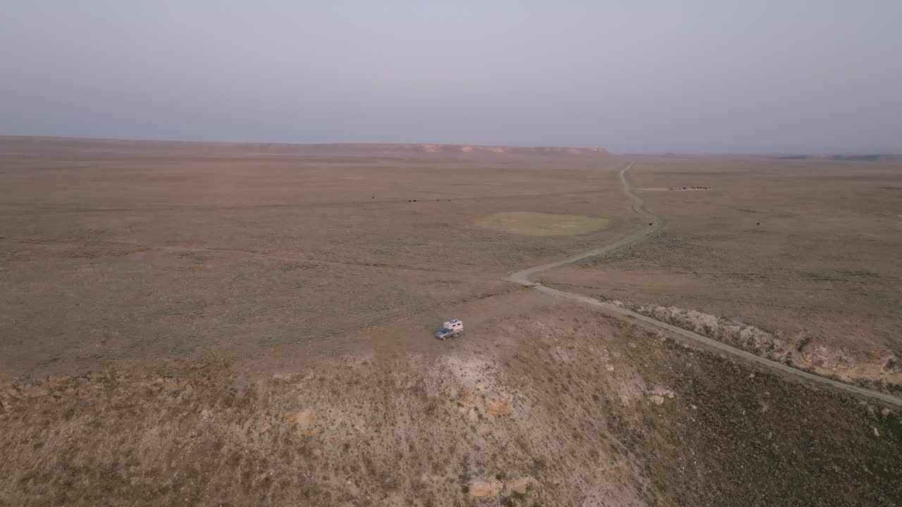 camionetas de campamento estacionan a lo largo de un camino de tierra remoto a través de un extenso paisaje desértico al anochecer