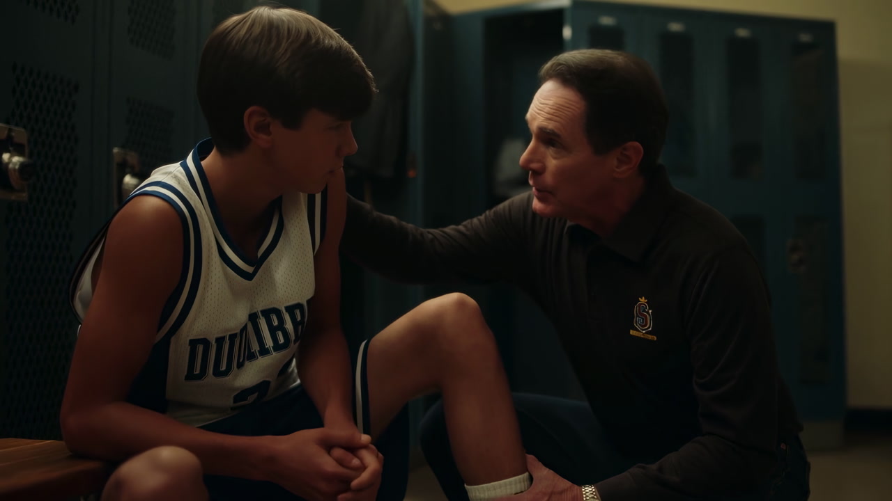Locker Room Coach Comforts Young Player Sitting On Bench, Coach Kneels, Hand On Shoulder, White Basketball