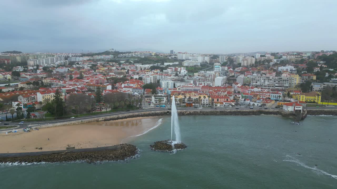 Flying at a cloudy day over the Atlantic Ocean with a view of the fountain in the sea towards the coast, with the village of Paço de Arcos in the background.Oeiras,Portugal