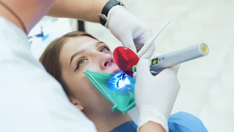 a dentist in white latex gloves uses an ultraviolet light tool to treat a tooth. a girl treats teeth for caries. visit to the dentist