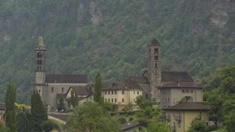 iglesia católica y torres en un pequeño pueblo rodeado de un denso bosque de pinos verdes, ladera verde en el fondo durante el día, alpes suizos