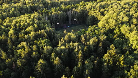 Disparo-De-Un-Dron-Inclinándose-Hacia-Un-Campo-De-Fútbol-En-Medio-De-Un-Bosque-Denso-E-Iluminado-Por-El-Sol.