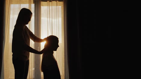 Silueta-De-Una-Madre-Peinando-El-Cabello-De-Su-Hija-En-La-Ventana