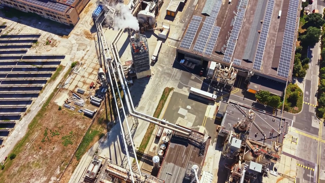 Sito industriale con pannelli solari e attrezzature di lavorazione, visto dall'alto di giorno in un'area urbana.