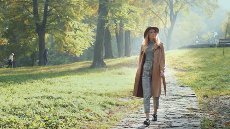 Vista-Completa-De-Una-Mujer-Caucásica-Con-Cabello-Rubio-Usando-Un-Abrigo-Y-Sombrero-Caminando-En-El-Parque-Por-La-Mañana-En-Otoño