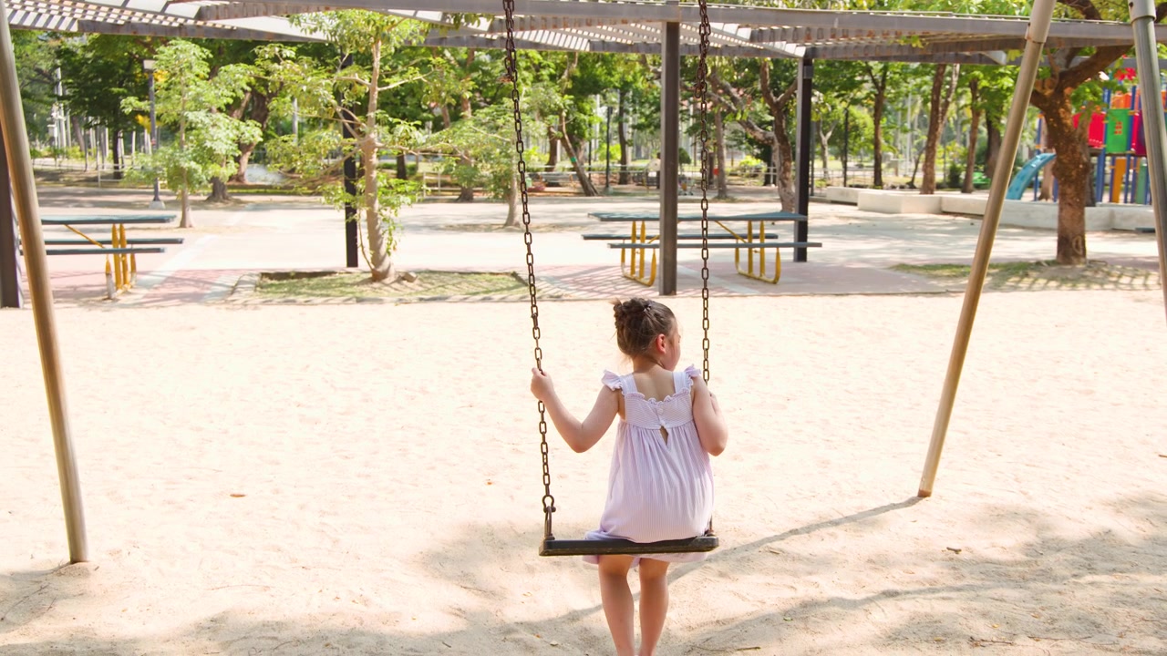 Una bambina con un vestito rosa si dondola su un parco giochi nel Parco Lumpini, Bangkok