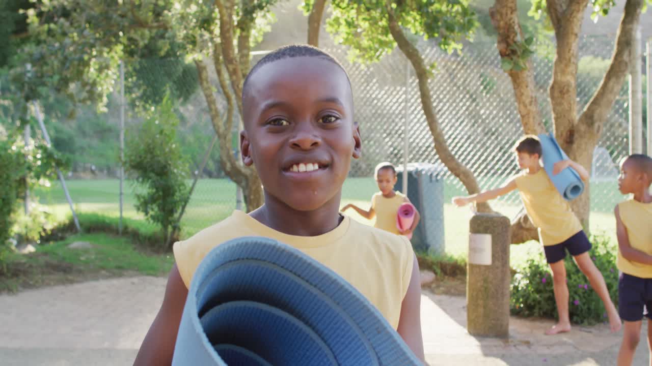 야외에서 요가 수업 후 요가 매트를 들고 있는 행복한 아프리카계 미국인 학교생의 초상화